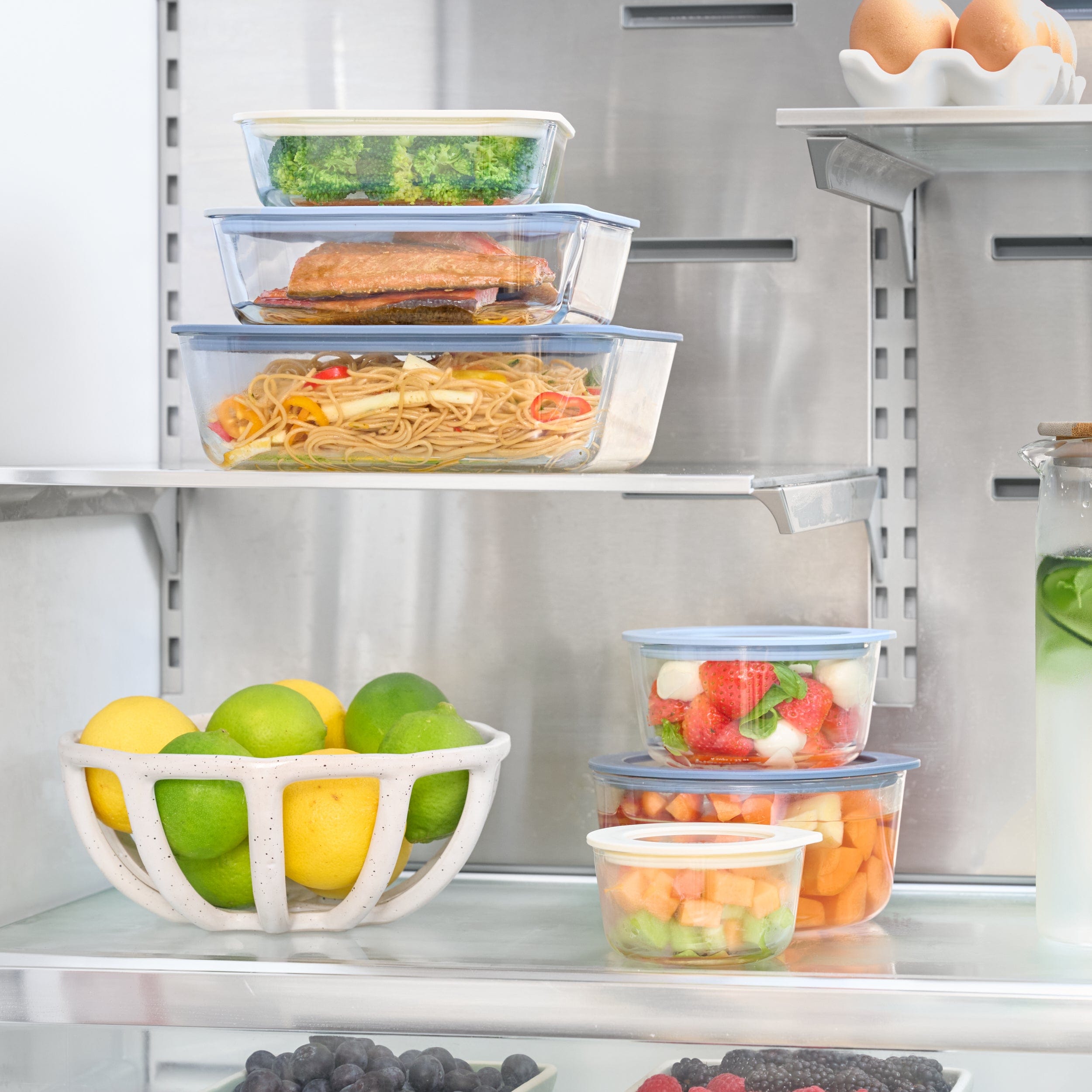 Set of glass containers arranged inside a fridge with leftovers, fruits and various groceries.