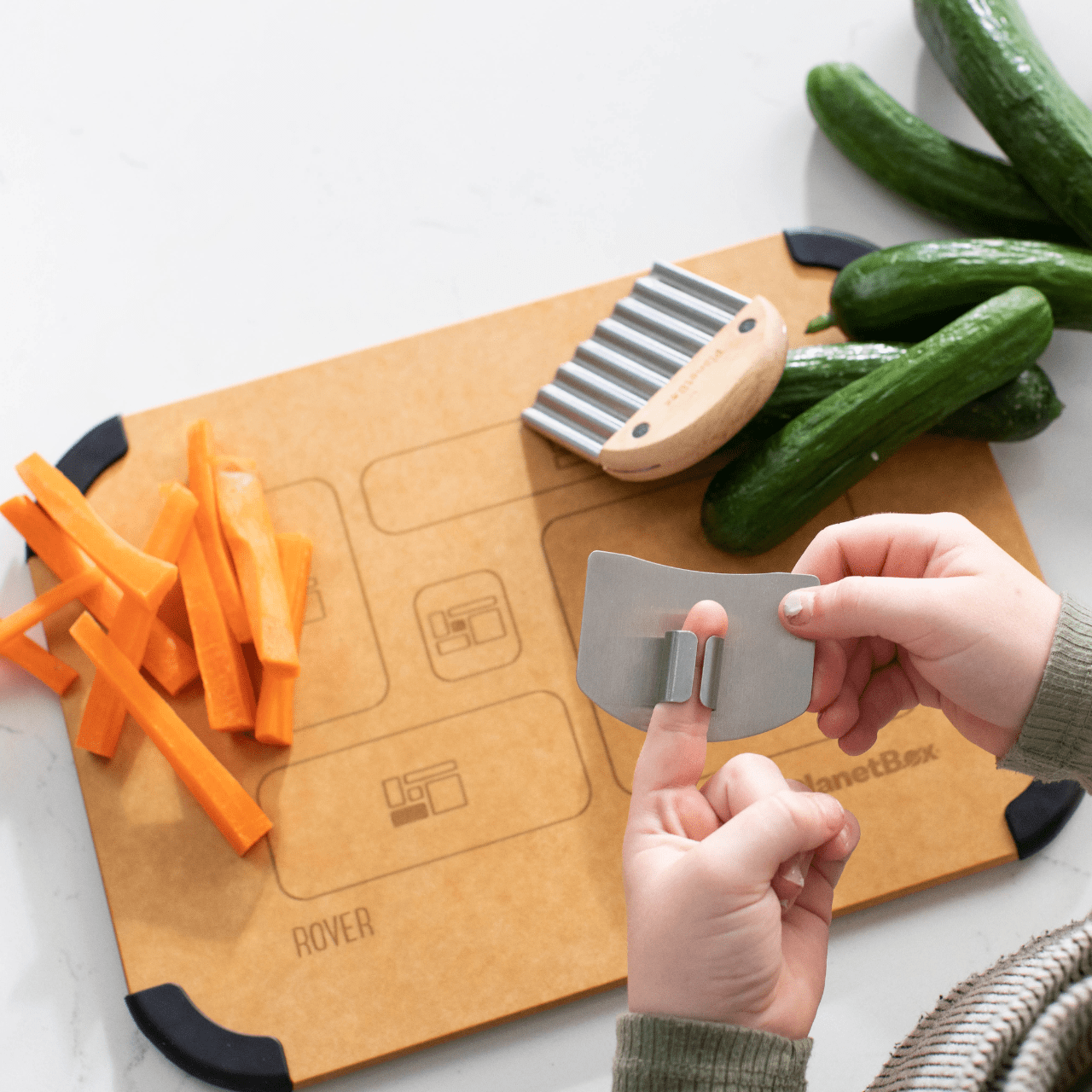 Child using finger guard included in Prep to Pack Three Piece set. In the background is the wavy chopper, cucumbers and carrot sticks.