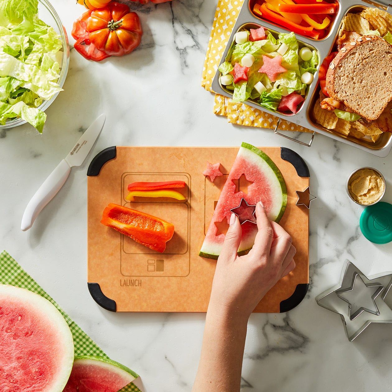 PlanetBox Prep to Pack cutting board with fruit and vegetables being prepared on top. 