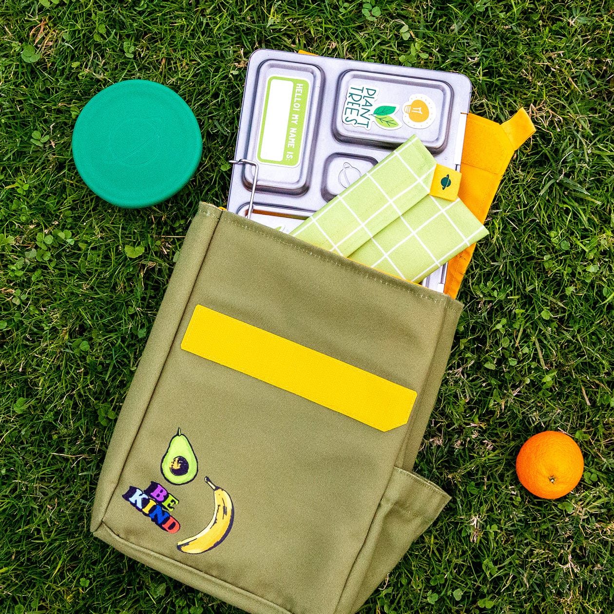 Green lunch sack laid in grass with content spilling from top.