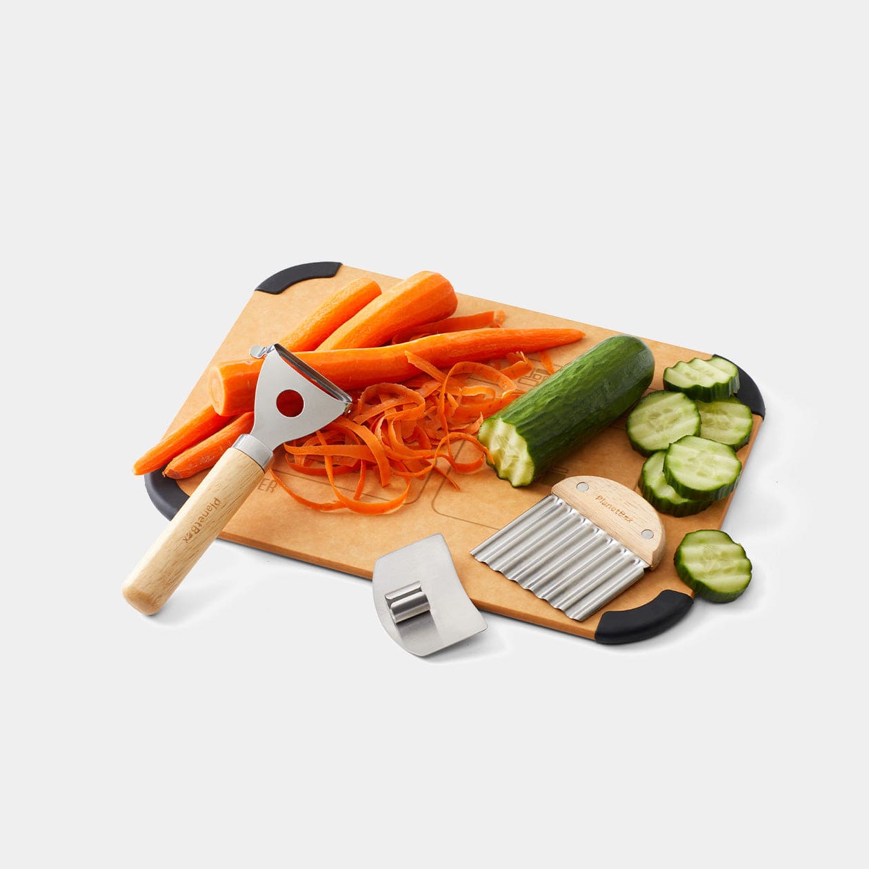 Prep to Pack Prep Set featured alongside the Prep to Pack cutting board. A peeled carrot rests on the board alongside a zucchini that has been wavy cut. The peeler, finger guard and wavy chopper are resting in the foreground. 